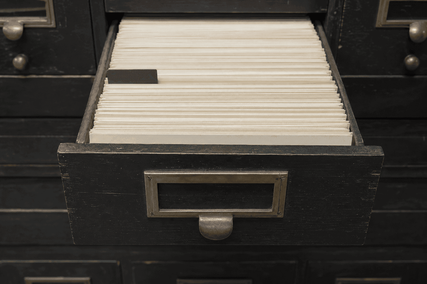 An open card-index drawer in a records office, packed with blank cream index cards and one green divider tab.